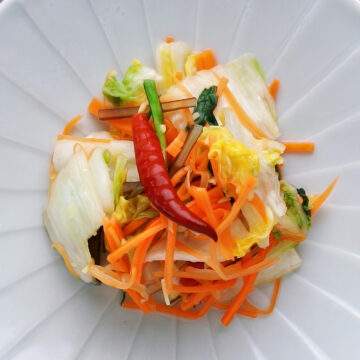 Colorful mound of asazuke on a plate. Crisp napa cabbage, sallions, and carrots glisten with a red chili adding a bold accent.