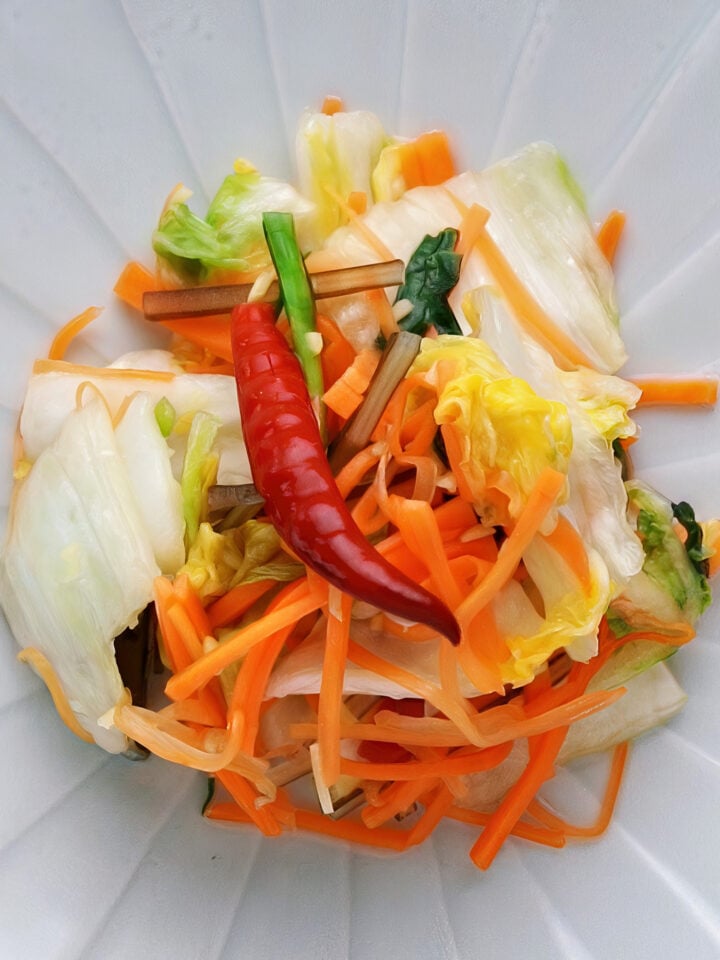 Colorful mound of asazuke on a plate. Crisp napa cabbage, sallions, and carrots glisten with a red chili adding a bold accent.