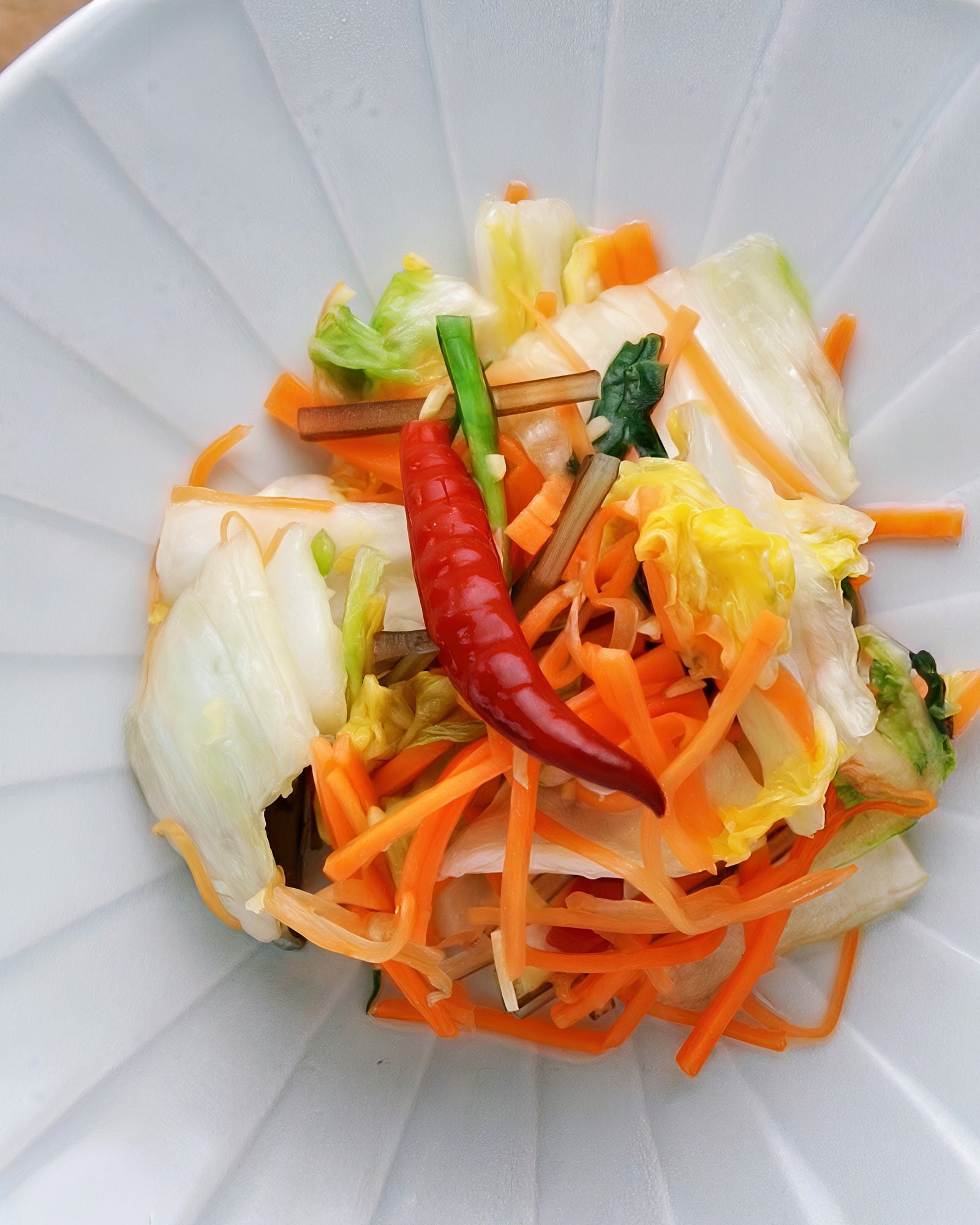 Colorful mound of asazuke on a plate. Crisp napa cabbage, sallions, and carrots glisten with a red chili adding a bold accent.