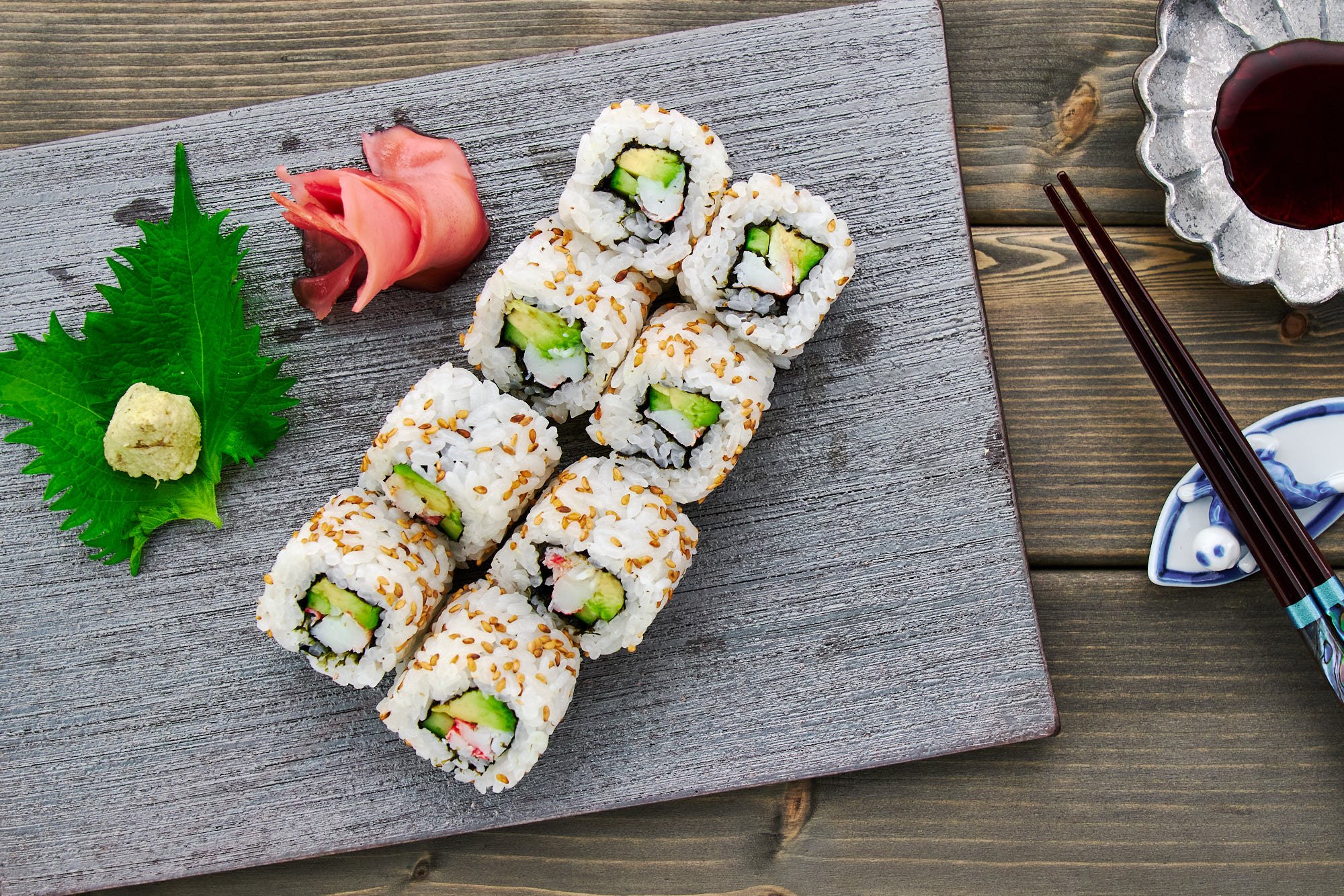 Overhead view of a plate of California roll served with wasabi, soy sauce and pickled ginger.