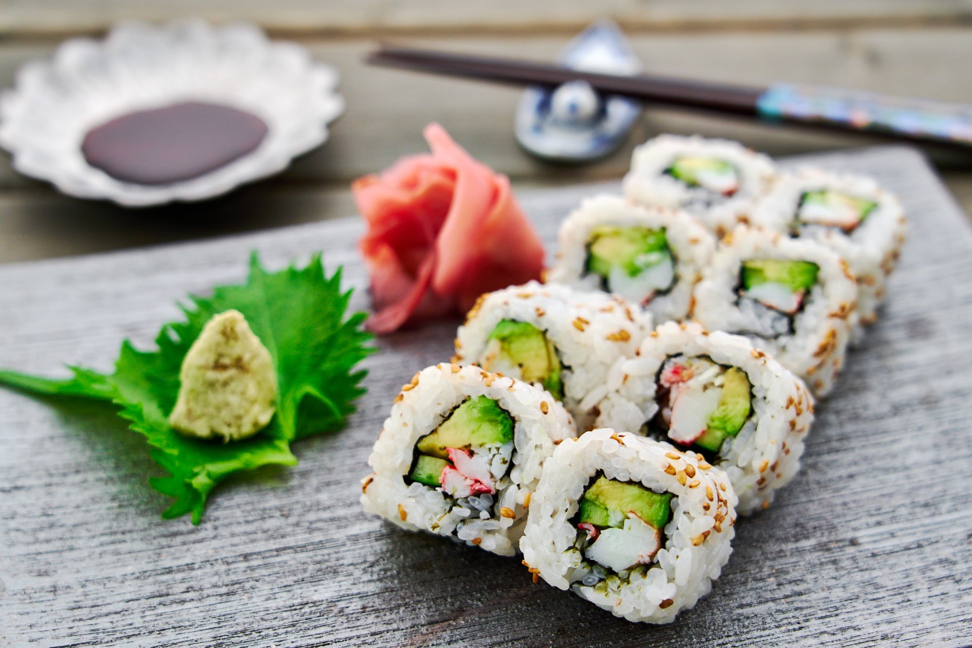 California sushi roll with avocado, crab, and cucumbers wrapped in tangy sweet sushi rice with wasabi and pickled sushi ginger in the background.