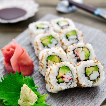 Closeup of a plate of homemade California rolls filled with crab, avocado and cucumber wrapped in tangy sushi rice and nori.