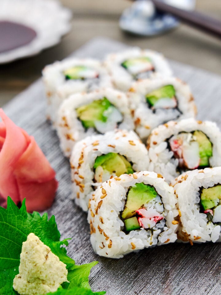 Closeup of a plate of homemade California rolls filled with crab, avocado and cucumber wrapped in tangy sushi rice and nori.