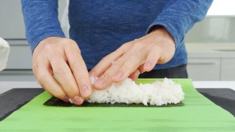 Spreading mound of sushi rice across a sheet of nori.