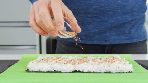 Sprinkling toasted sesame seeds onto sushi rice.