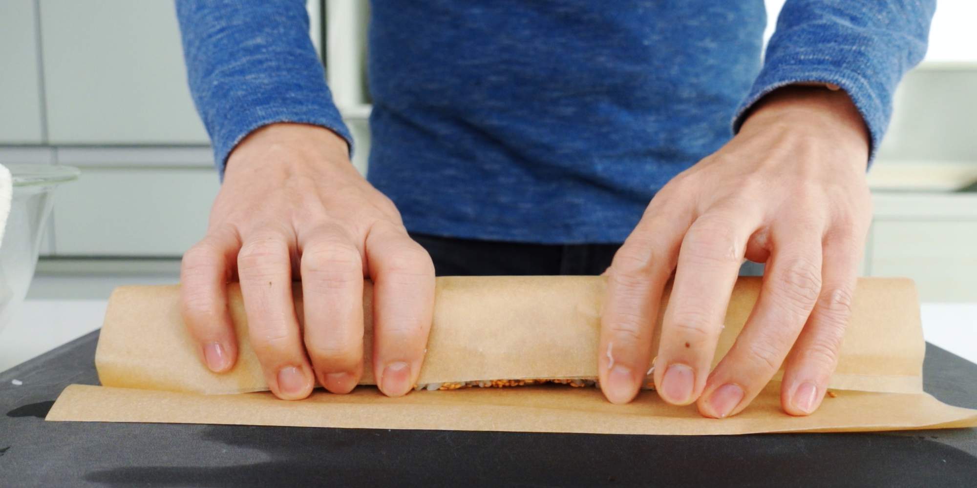Rolling a sushi roll with parchment paper.