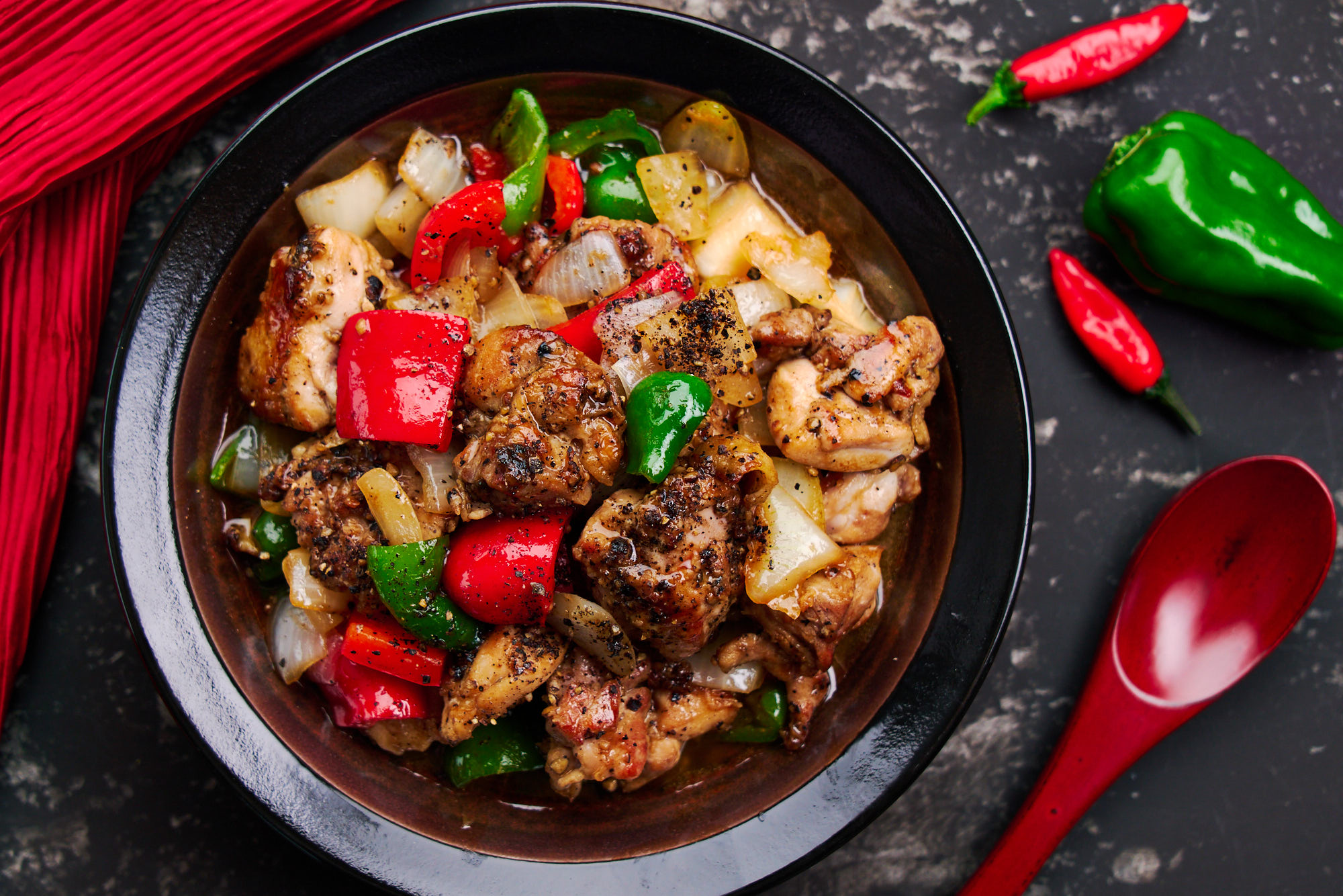 Overhead view of a bowl of black pepper chicken with peppers, onions and big hunks of juicy chicken in a spicy black pepper sauce.