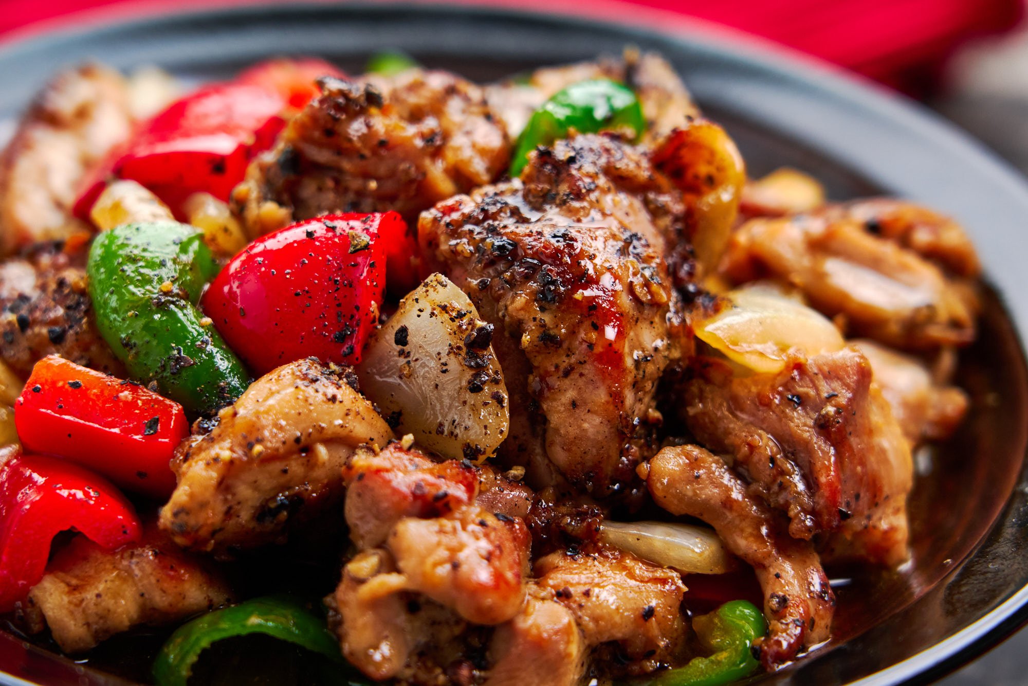 Closeup of a bowl of chicken stir fried with vegetables and black pepper sauce.
