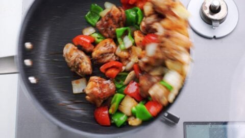 Tossing black pepper chicken in a frying pan with oyster sauce.