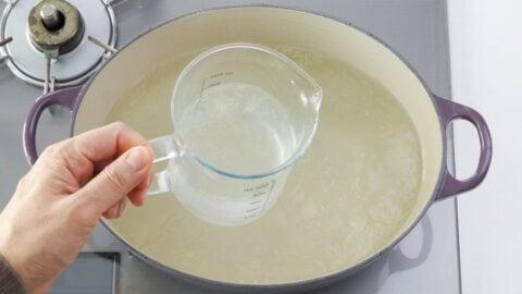 Reserving pork boiling liquid from a pot in a glass measuring cup.