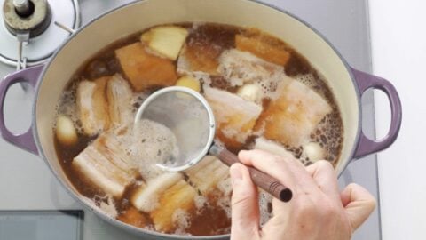 Skimming scum off the surface of the braising liquid.