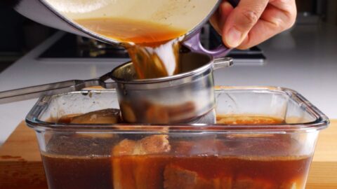 Straining braising liquid into pork belly kakuni.