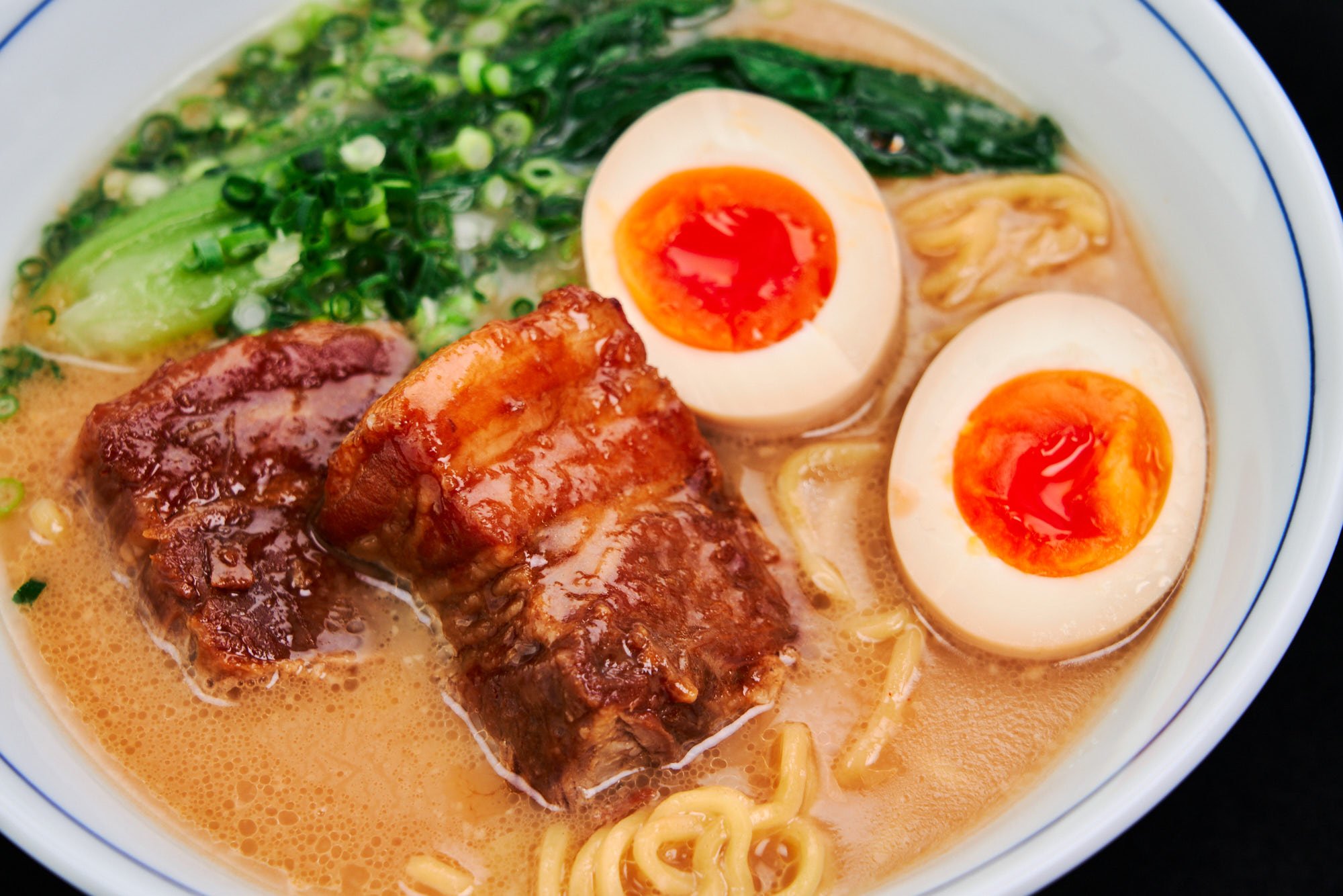 Rich, velvety ramen is crowned with braised pork belly, jammy soft-boiled eggs, fresh scallions, and bok choy, all bathed in a deeply flavorful, umami-packed broth.