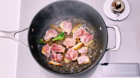 Chicken and scallions in a pan being deglazed with sake.