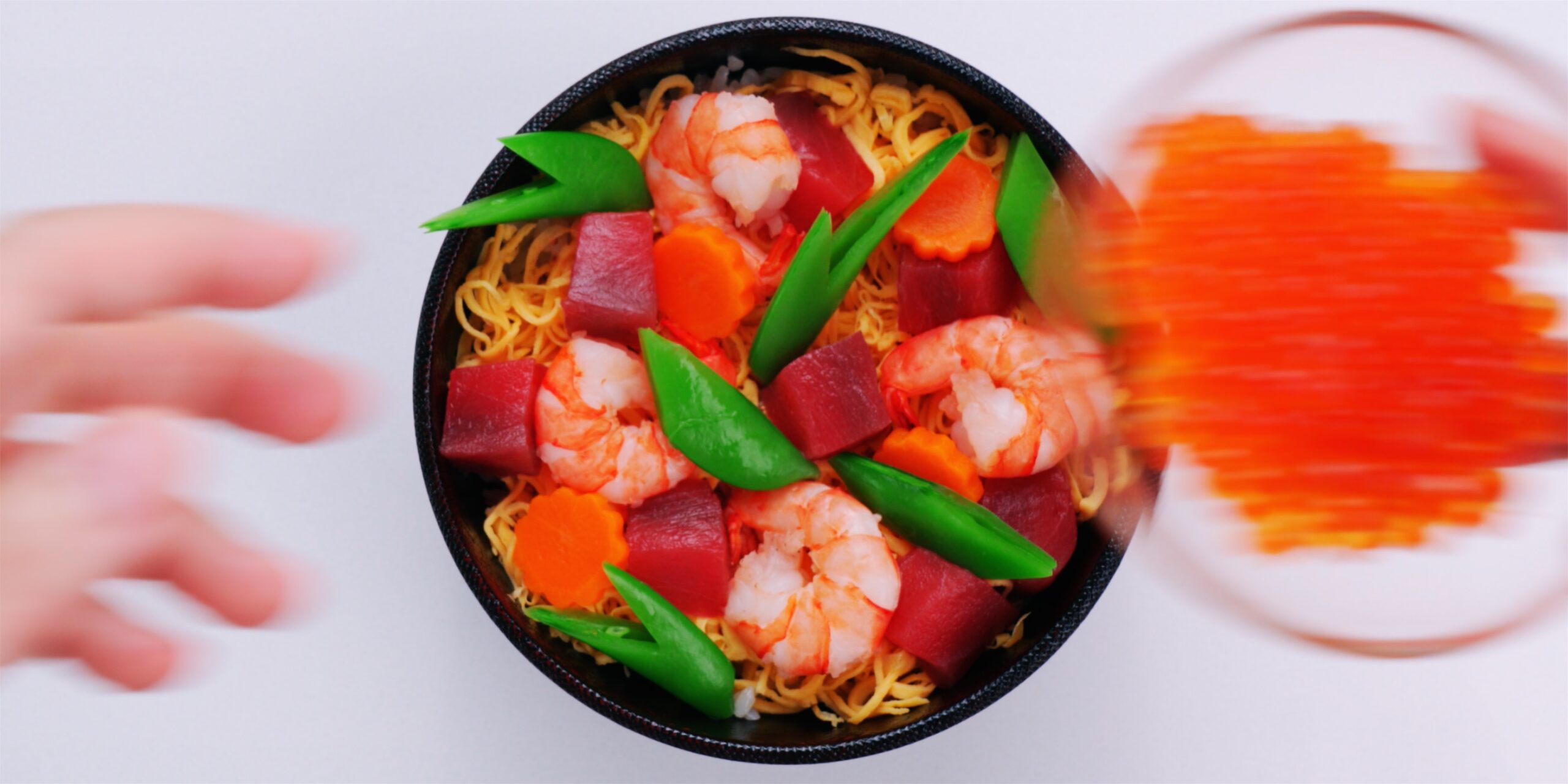 Chirashi sushi bowl topped with tuna, shrimp, eggs, carrots and snap peas.