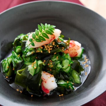 Plated sunomono salad with crab and sesame seeds glows under soft light, inviting with its glossy textures and vivid greens.