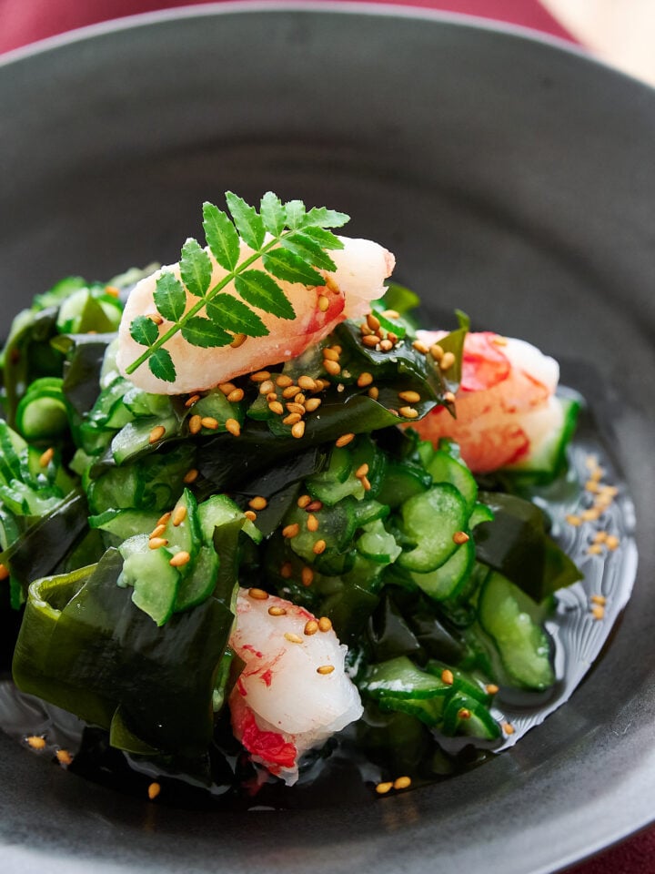 Plated sunomono salad with crab and sesame seeds glows under soft light, inviting with its glossy textures and vivid greens.