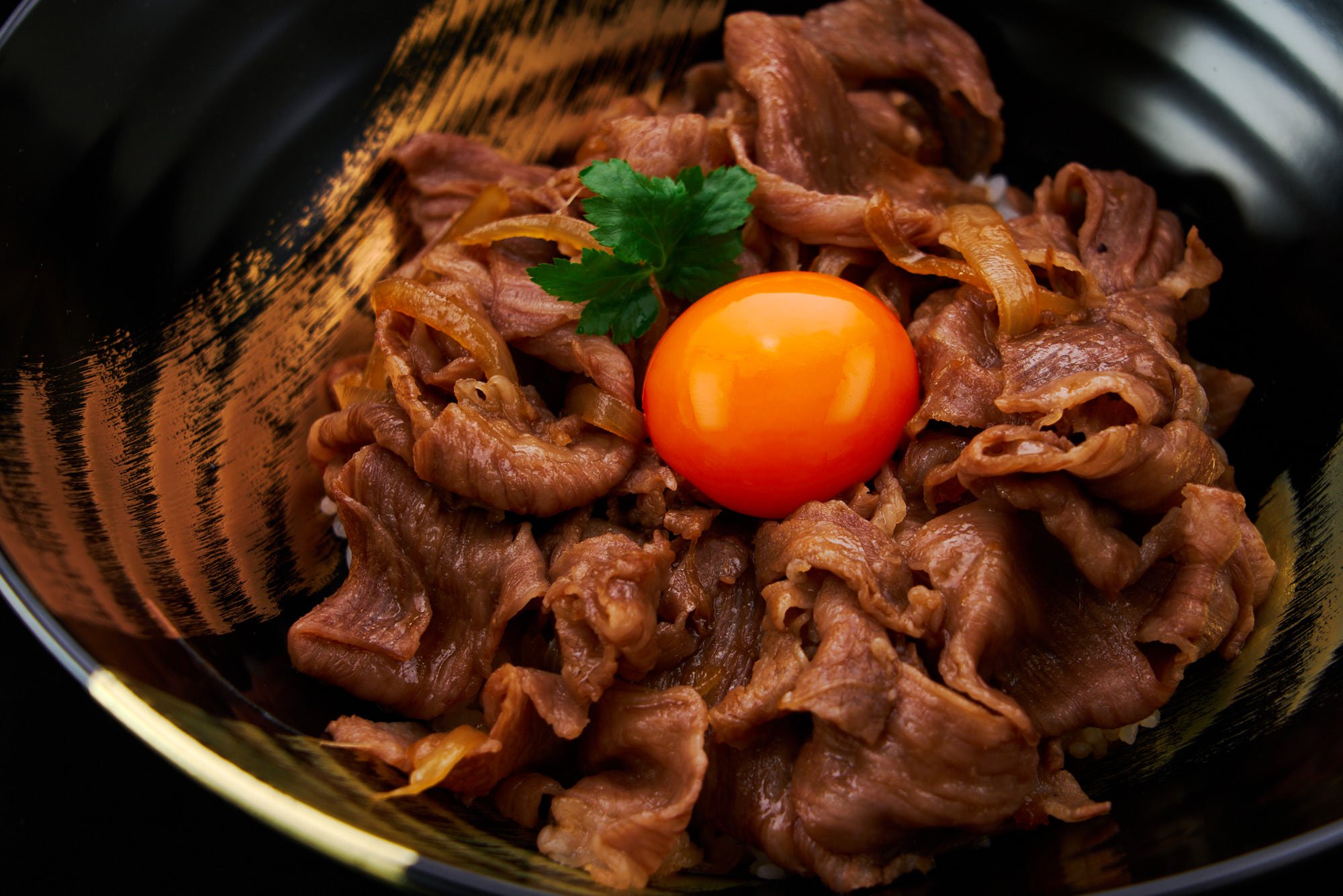 Japanese beef bowl or gyudon is served on a fluffy bed of short-grain rice with a golden egg yolk gleaming like a jewel on top.
