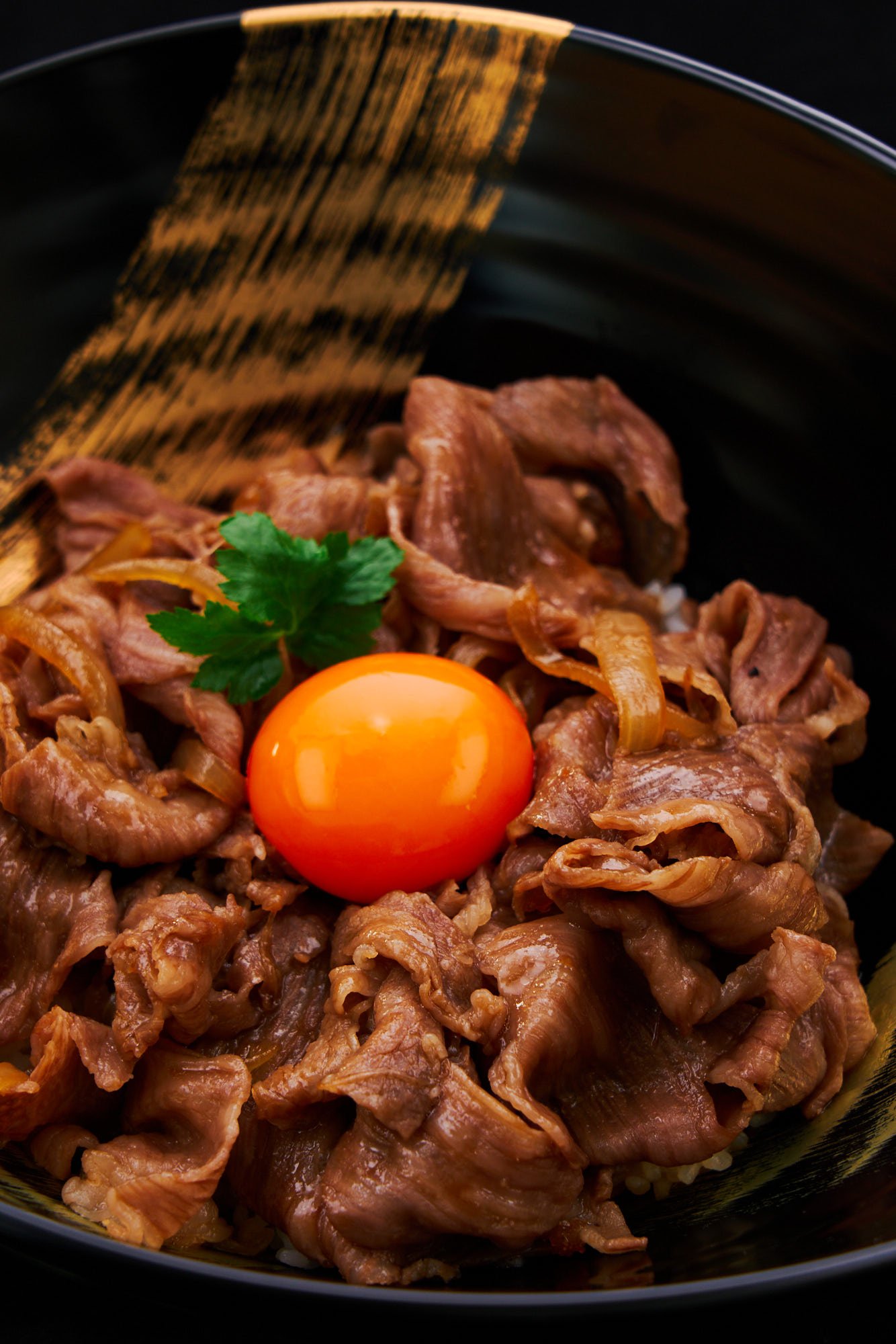 Japanese gyudon or beef bowl with melt-in-your-mouth wagyu beef, perfectly cooked with a savory gyudon sauce that clings to each slice. Topped with a vibrant orange egg yolk.