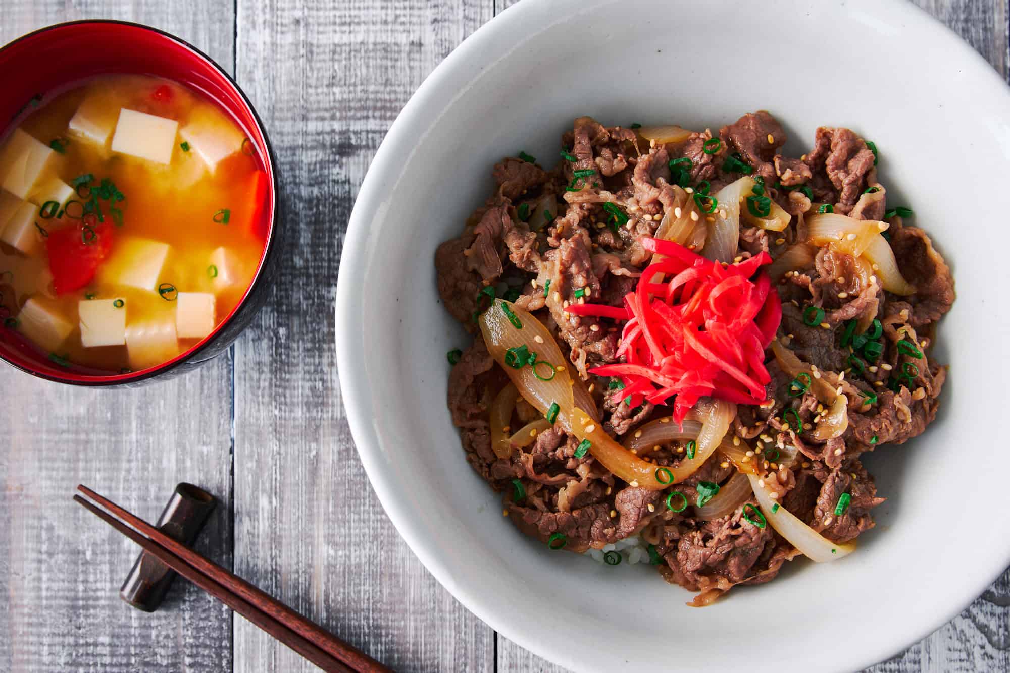 Overhead view of a bowl of beef gyudon, along with miso soup and chopsticks.