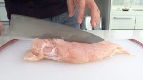 Pounding chicken breast with the back of a knife.