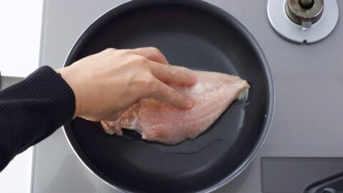 Placing a chicken breast in the pan with the skin-side down.