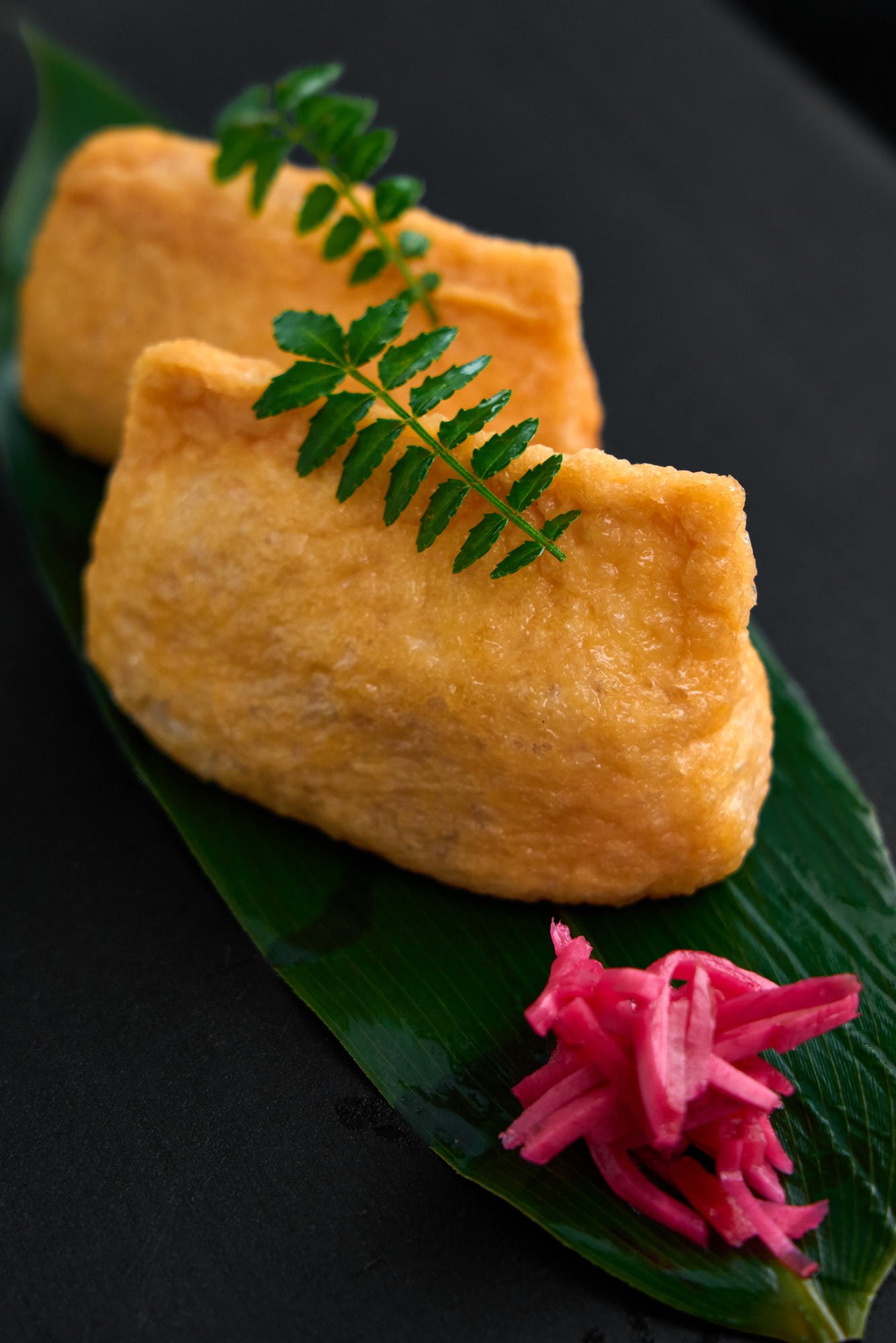Classic inari sushi—sweet-simmered tofu pockets filled with tangy sushi rice. Garnished with kinome and served with pickled ginger for a clean, traditional presentation.