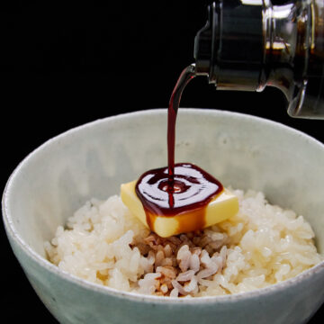 A savory drizzle of soy sauce pouring onto melting butter and hot rice, creating the ultimate bowl of comforting Japanese butter rice.