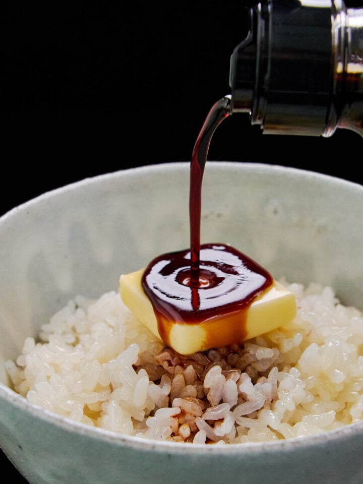 A savory drizzle of soy sauce pouring onto melting butter and hot rice, creating the ultimate bowl of comforting Japanese butter rice.