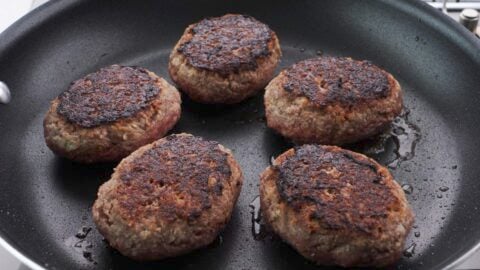 Browned hamburg steak patties in a frying pan.