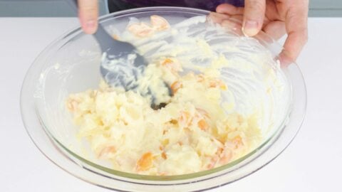 Mixing cooked potatoes and carrots into Japanese mayonnaise dressing.