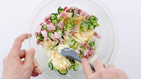 Mixing Japanese potato salad together in a glass bowl with a spatula.
