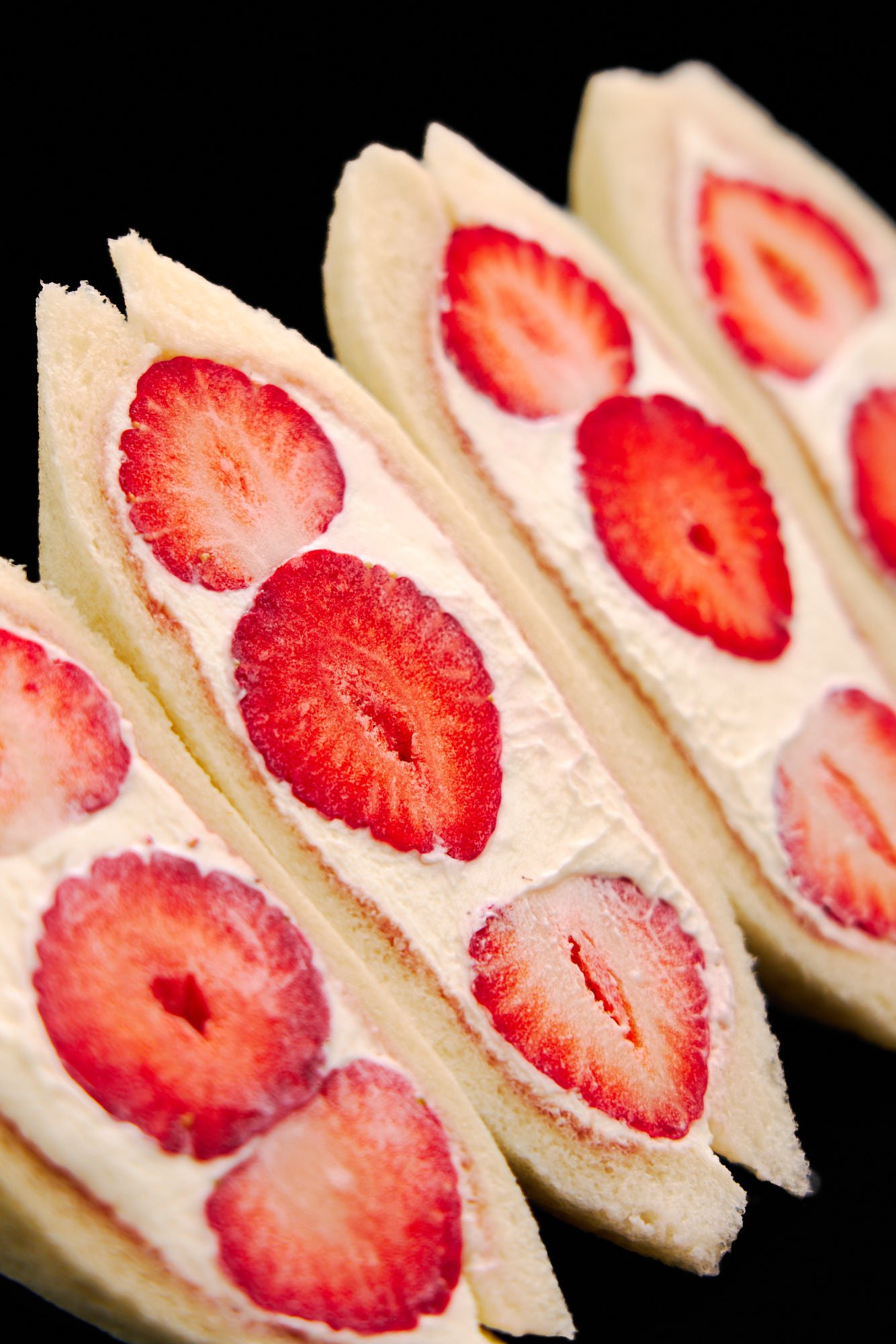 An enticing close-up of Japanese strawberry sandwich slices, highlighting juicy strawberries cushioned in pillowy whipped cream and tender milk bread.
