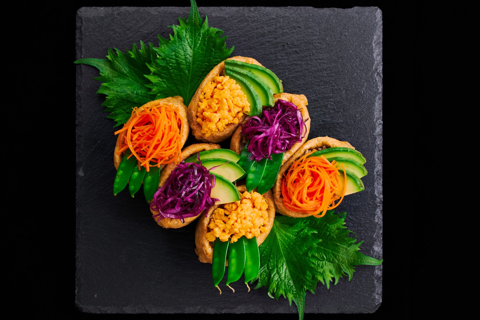 Inari sushi decorated with colorful toppings such as shredded carrots, egg, avocado, and pickled red cabbage.