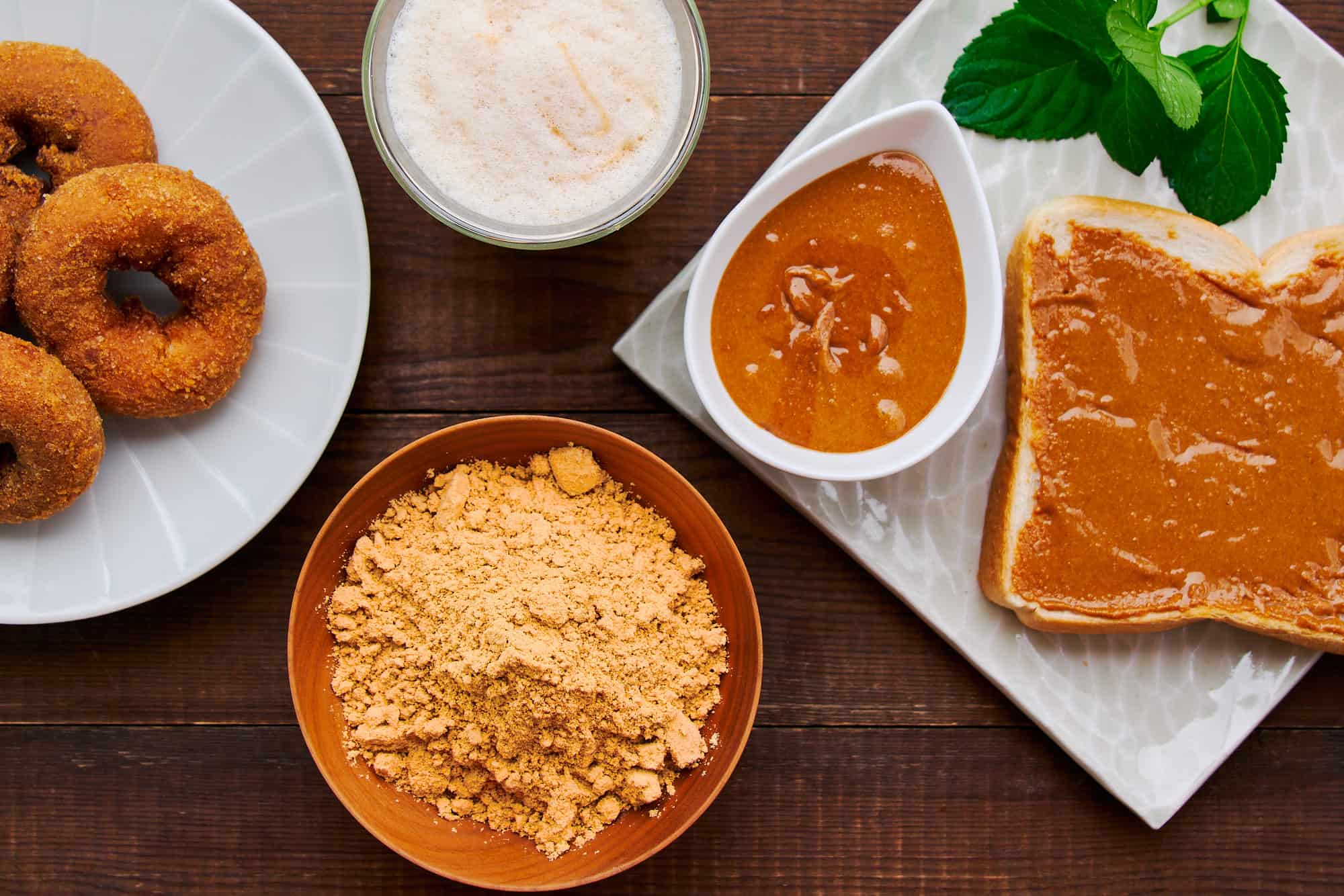 Overhead view of doughnuts generously dusted with kinako, creamy kinako butter spread lavishly on a slice of toasted bread, and a kinako latte. Just a few modern spins on this nutty Japanese ingredient.
