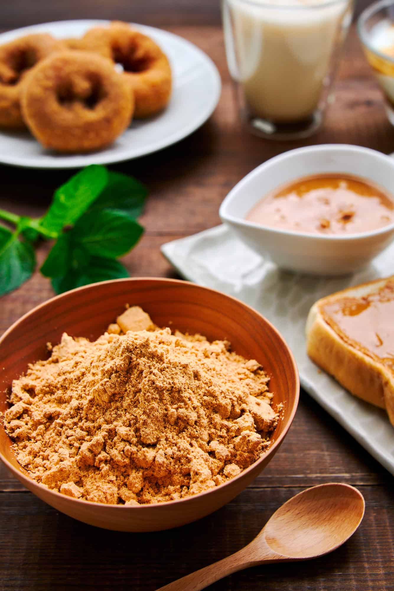 A vibrant spread featuring a bowl of kinako, or roasted soybean powder, kinako-dusted doughnuts, kinako butter on toast, and a kinako latte, illustrating the myriad uses of this traditional Japanese ingredient.