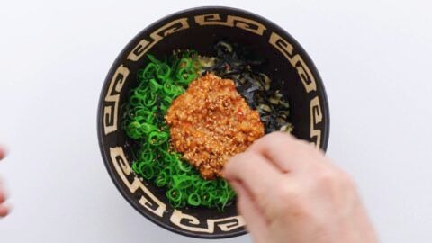Sprinkling toasted sesame seeds on a bowl of mazesoba.