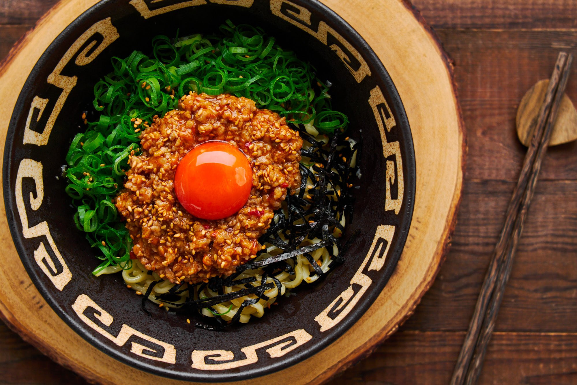 Overhead view of a bowl of mazemen (mazesoba). Soupless ramen noodles topped with spicy pork, scallions and an egg yolk.