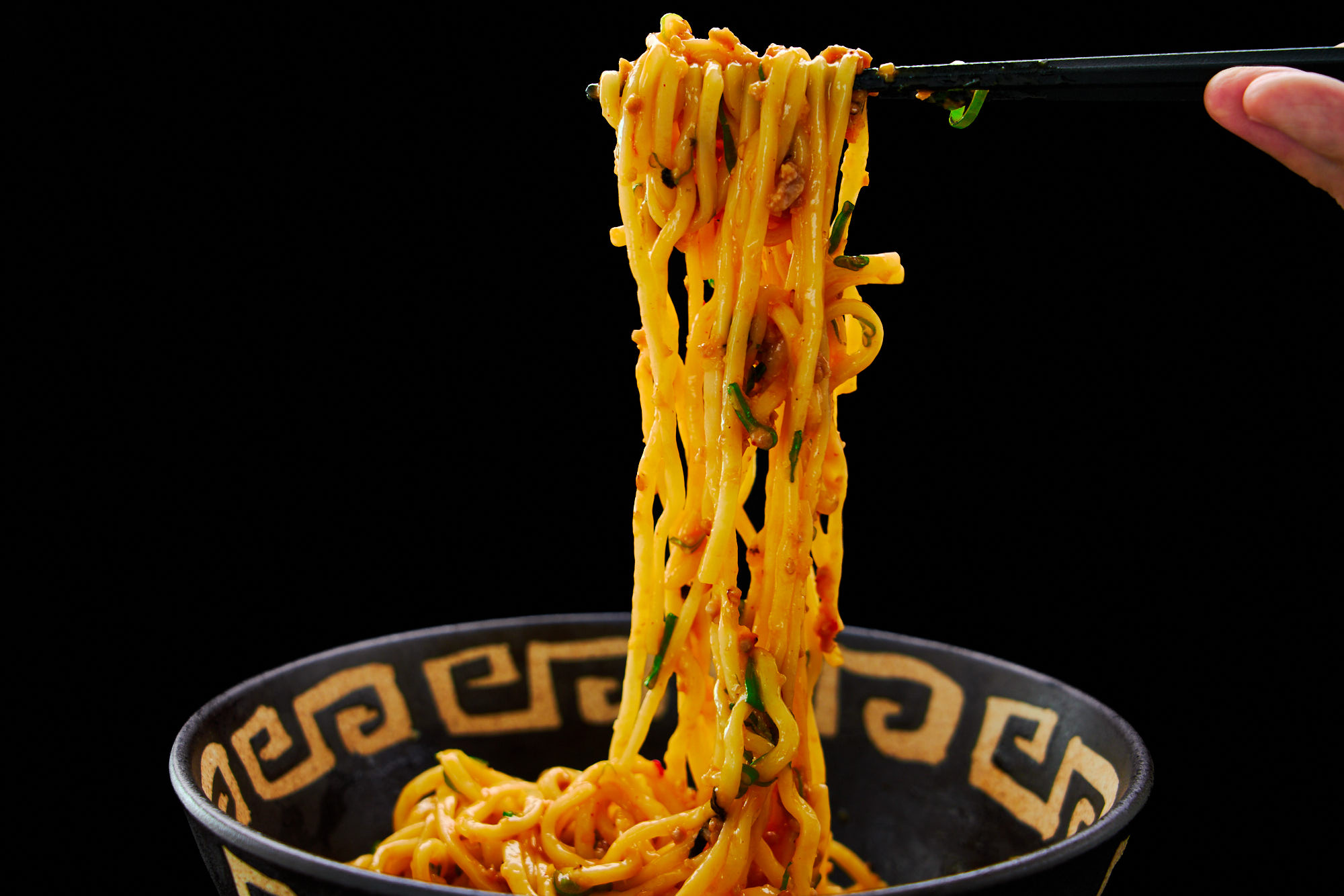 Pulling mazesoba ramen noodles glazed with aromatic scallion oil and spicy pork from a bowl with chopsticks.