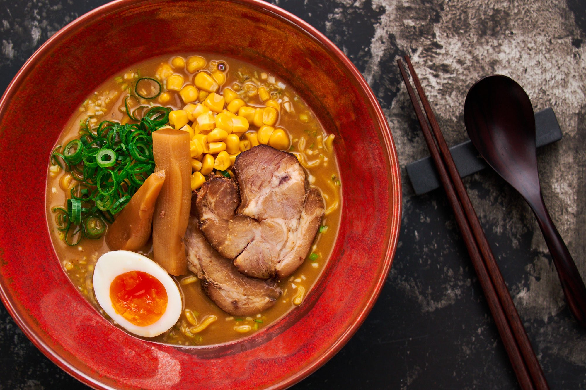 A top-down view of miso ramen with layers of ingredients including sweet corn, bamboo shoots, and green onions, balanced perfectly with a rich broth.