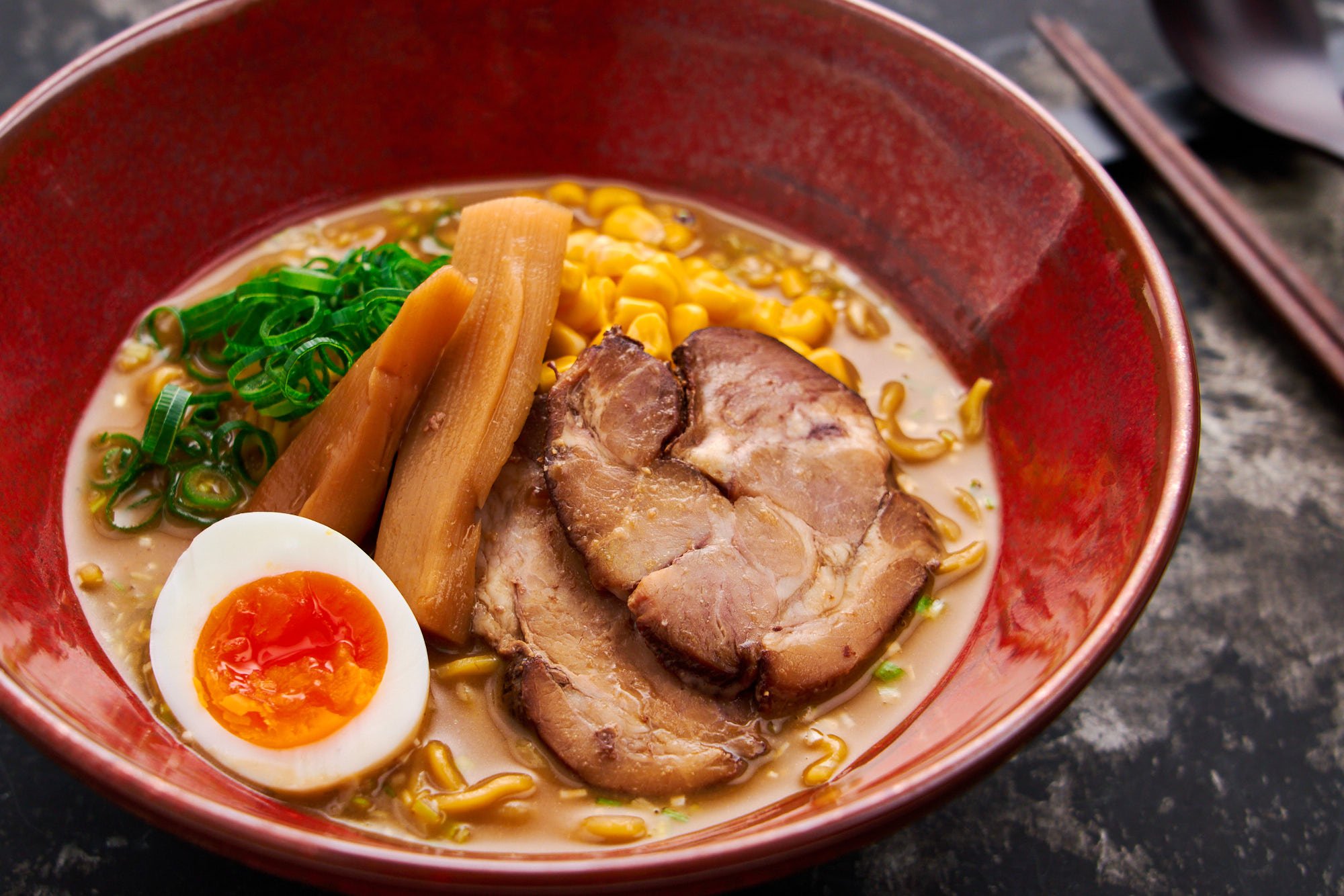 Rich, savory miso ramen garnished with juicy pork slices, a golden ajitama egg, and fresh green onions, ready to enjoy.