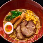 A close-up of Sapporo-style miso ramen, highlighting the luscious broth, tender pork slices, and vibrant toppings like corn and green onions.