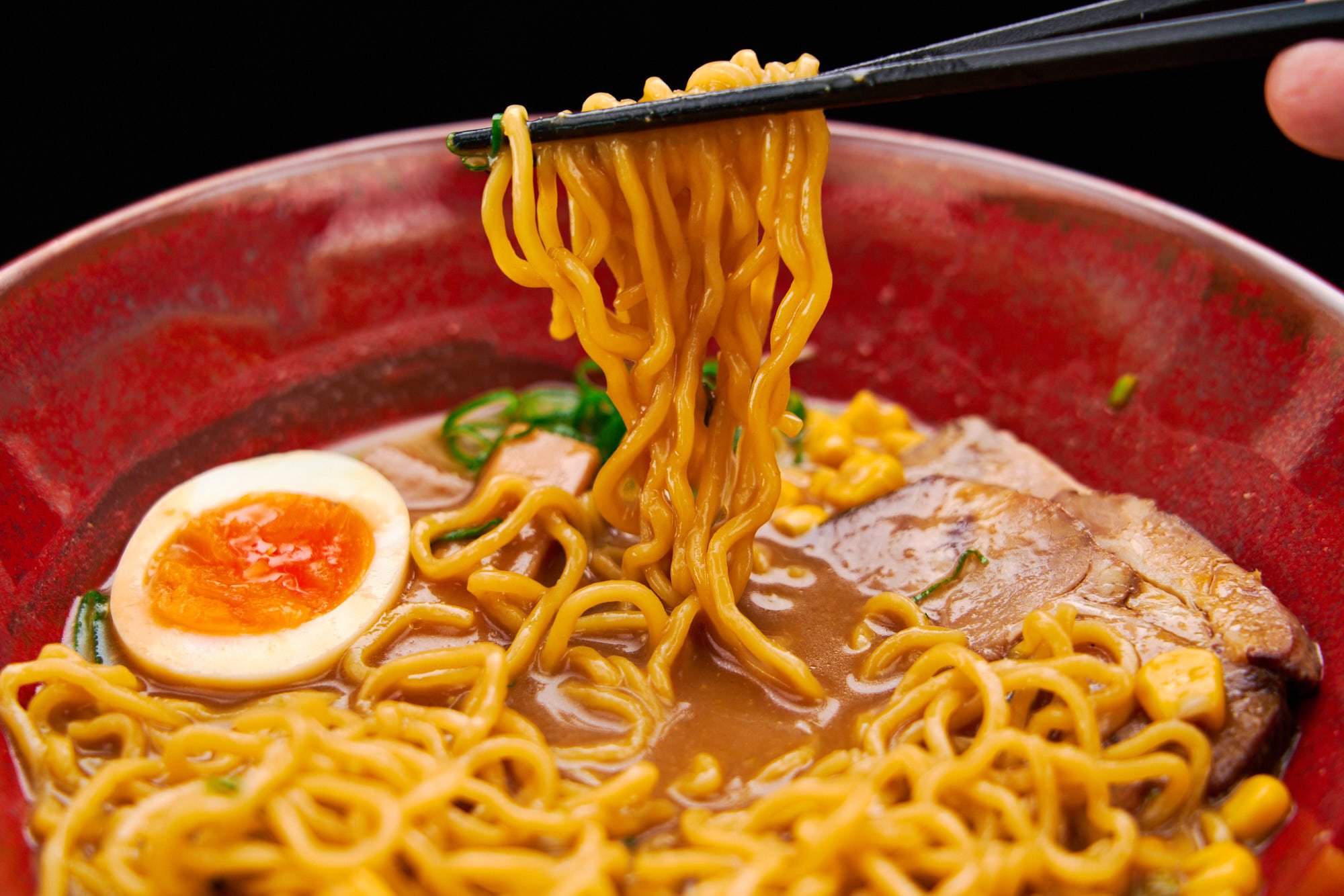 A tangle of golden, springy ramen noodles being pulled up from a bowl of rich miso ramen broth.