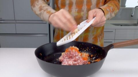 Grating aromatics into pan on a scale.