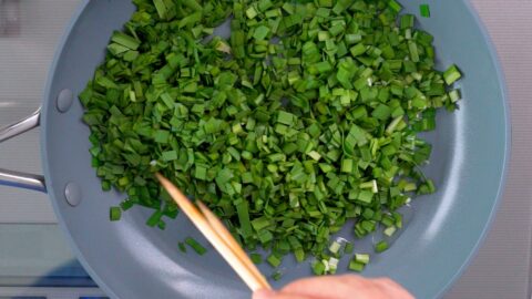 Sauteeing Nira (garlic chives) in a frying pan.