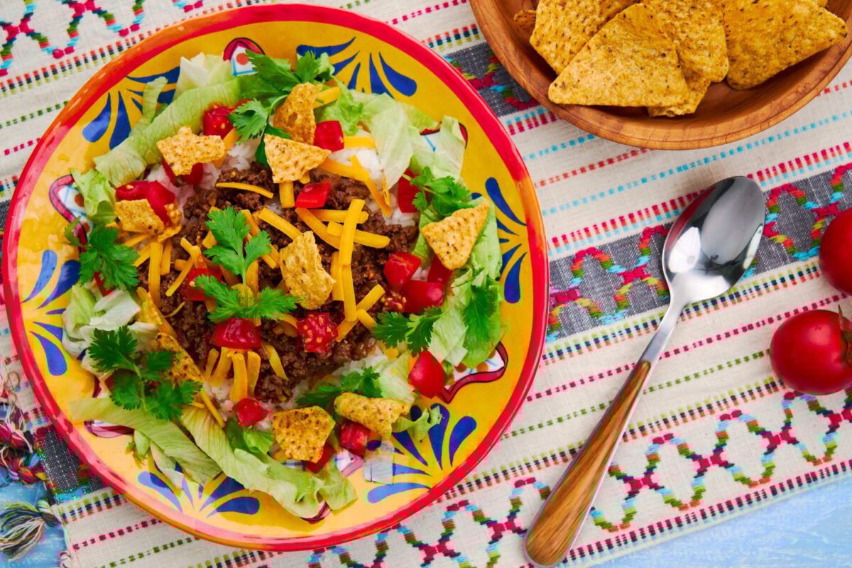 A plate of Okinawan Taco Rice with taco meat, and cheese over rice. Garnished with lettuce, tomatoes, and tortilla chips.