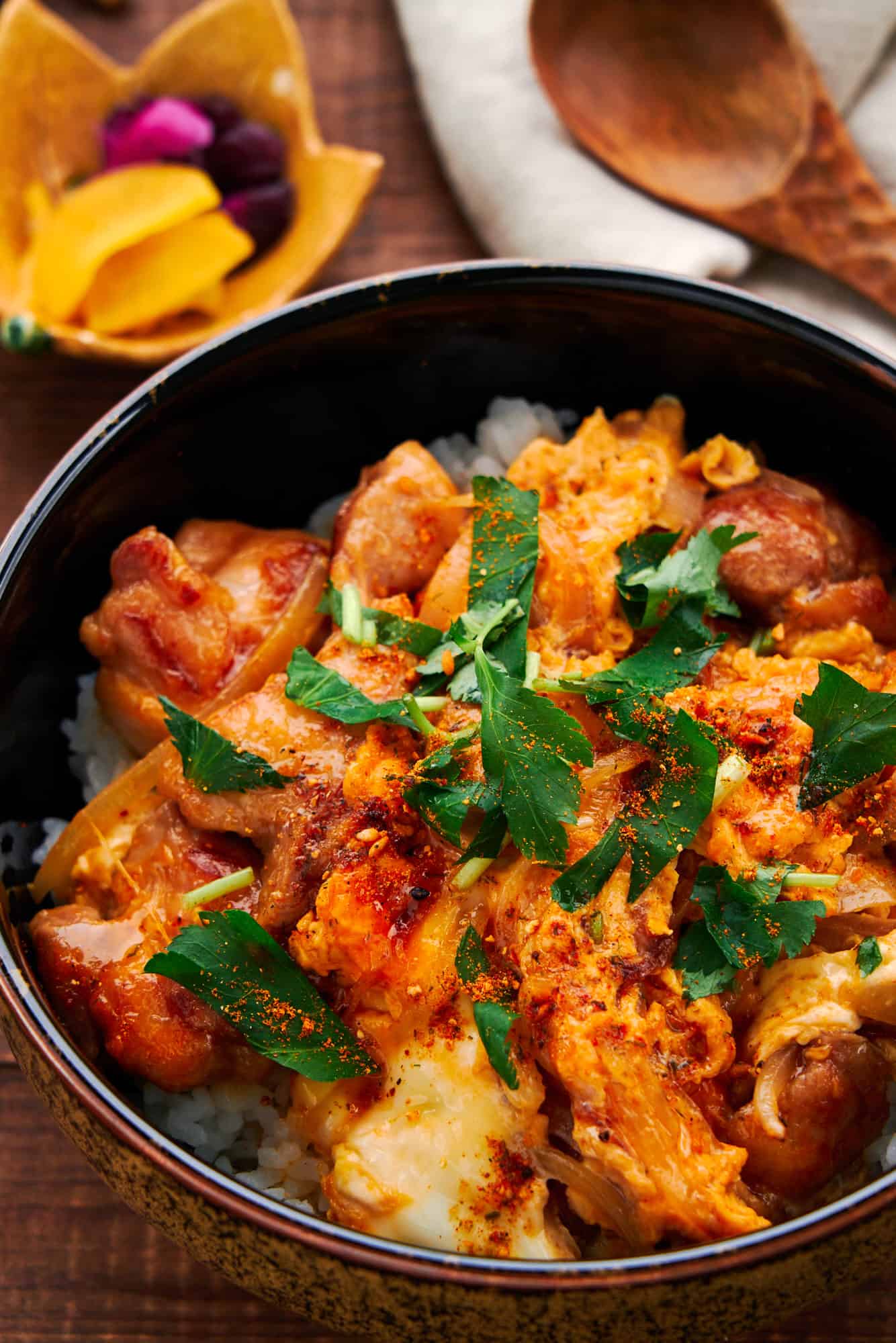 Bowl of Japanese Oyakodon, highlighting the intricate interplay between the velvety egg and juicy chicken pieces all over a bowl of rice.