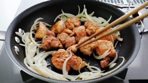 Flipping browned chicken over surrounded by onions.