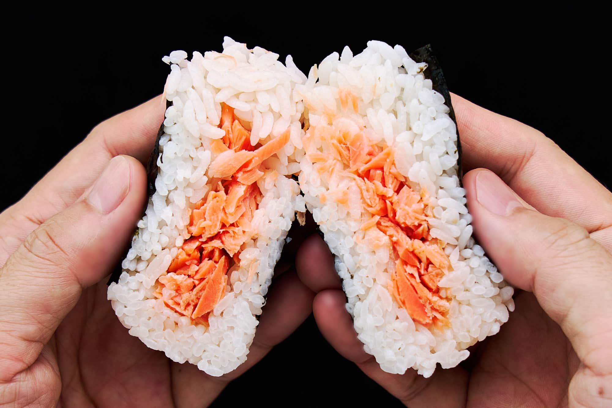 Salmon Onigiri split in half showing tender salted salmon flakes wrapped in a fluffy layer of Japanese short grain rice.
