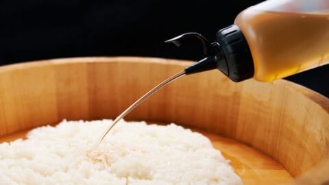 Savory, sweet, and sour seasoned sushi vinegar flows from a squeeze bottle onto a mound of Japanese sushi rice.
